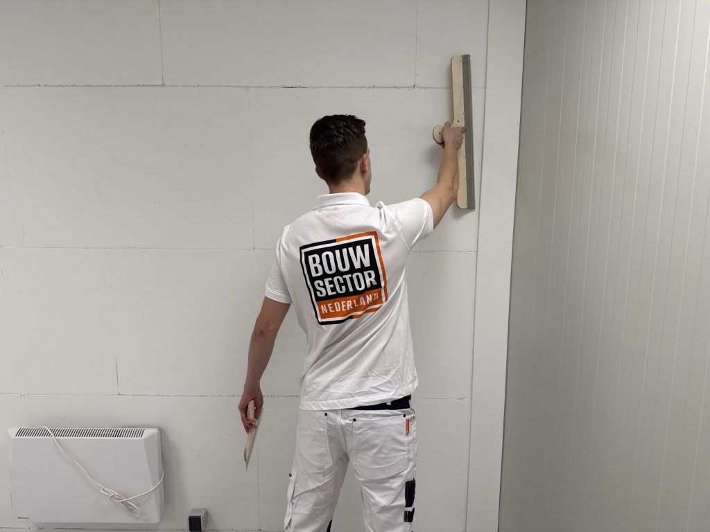 Stukadoor van Bouwsector Nederland met zijn rug naar de camera werkt een wand af met een lange spaan