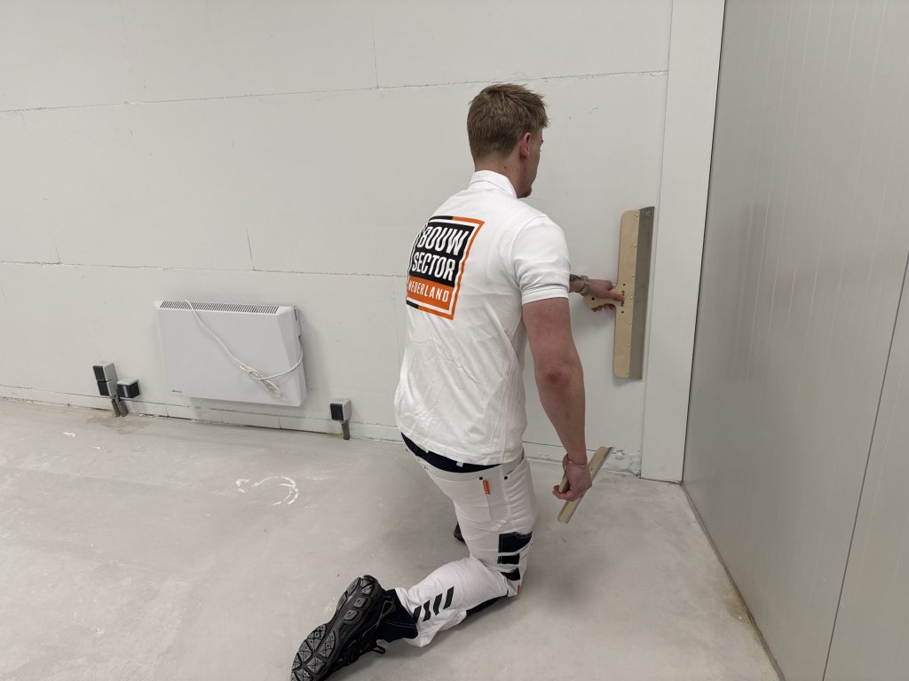 Stukadoor van Bouwsector Nederland zit op een knie en trekt het onderste deel van een wand vlak