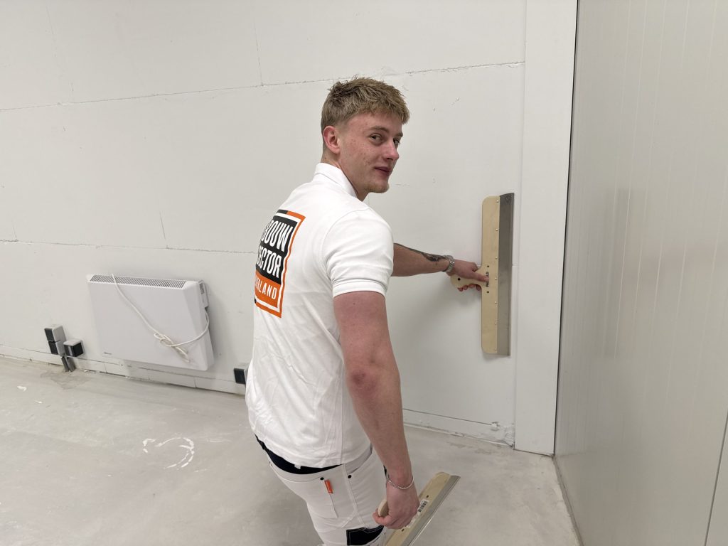 Stukadoor van Bouwsector Nederland met een lange spaan tegen de wand en een tweede spaan in de andere hand