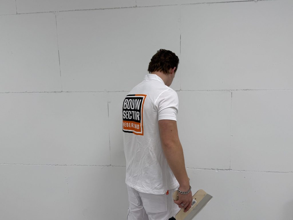 Stukadoor van Bouwsector Nederland bekijkt een kale wand van gipsblokken, met een plakspaan in zijn hand